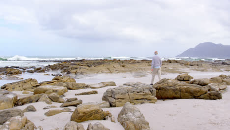 rear view of old caucasian senior man walking over rocks at beach 4k