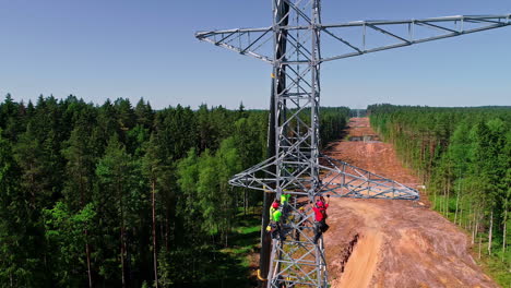 drone shot of worker climbing and build new electricity pylon in forest woodland during sunny day