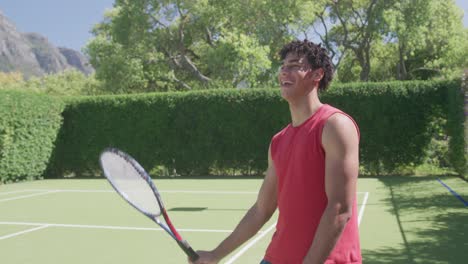 happy biracial man with tennis racket laughing in garden on sunny day