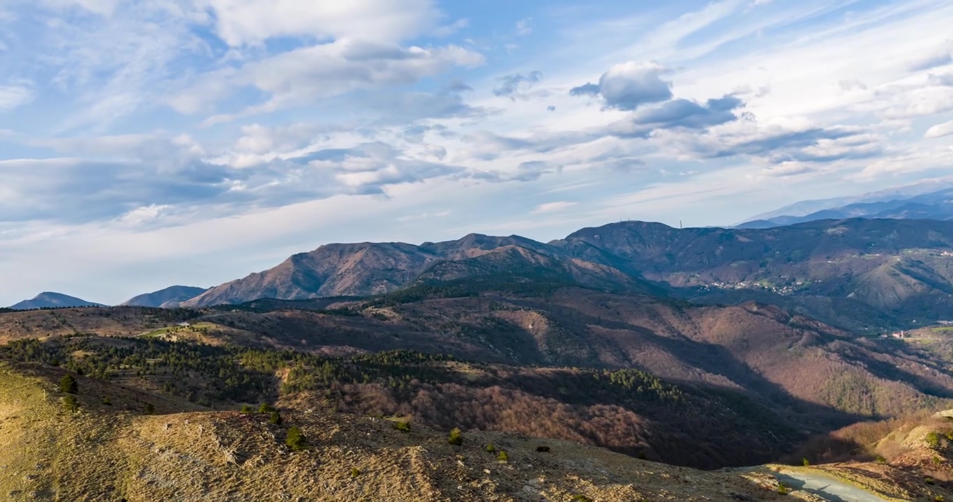Praglia, hyperlapse con un giro aéreo dinámico sobre escarpadas crestas montañosas y un sendero sinuoso, revelando amplias vistas panorámicas del valle bajo nubes dramáticas.