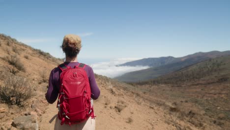 Una-Joven-Excursionista-Camina-Por-Un-Sendero-De-Montaña-En-El-Parque-Con-Vistas-A-Las-Nubes-Debajo.