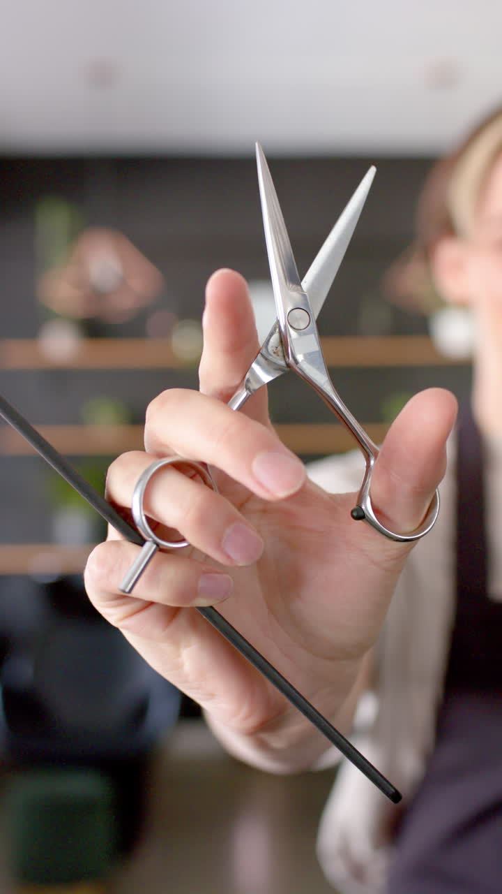 Vertical video of caucasian female hairdresser holding scissors and comb, in slow motion