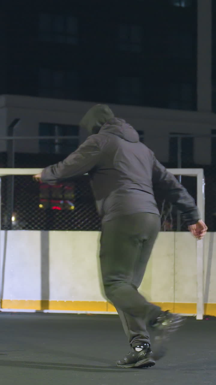 Athlete skillfully kicks soccer ball into goalpost during night practice on urban outdoor field, residential building in background and illuminated setting