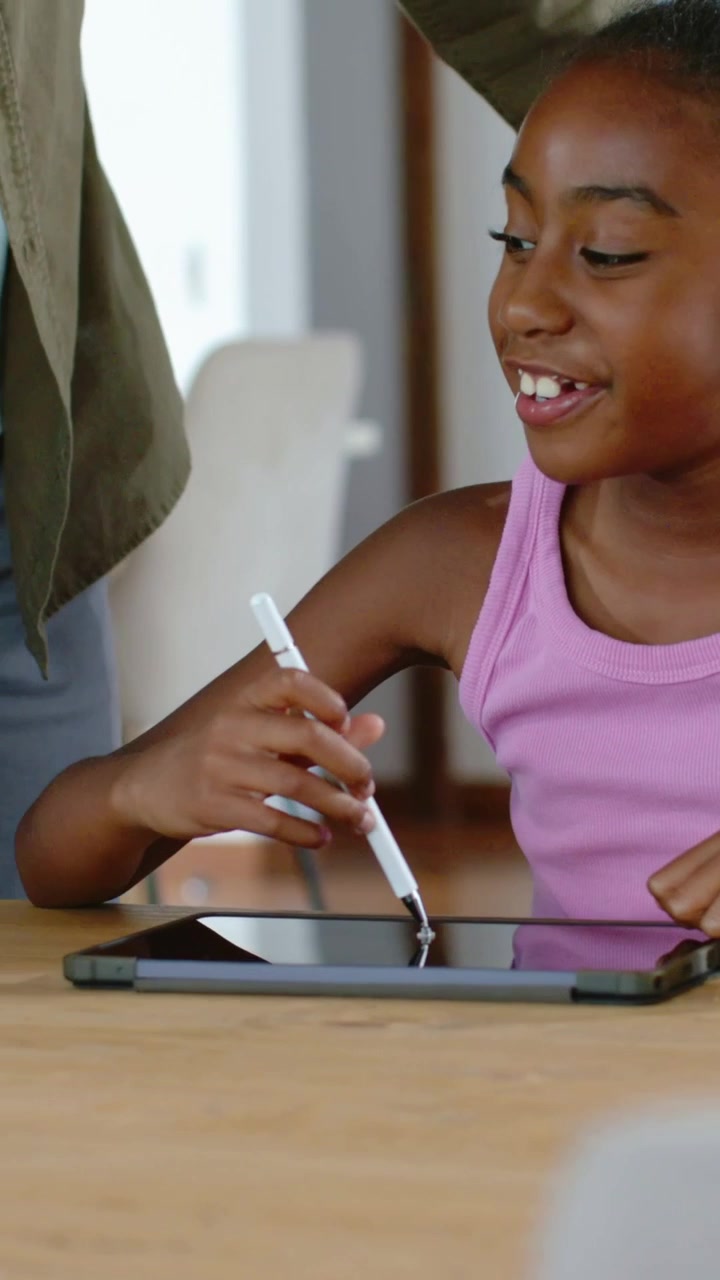 Video verticale: Ragazza che tocca lo stilo sul tablet, con un genitore che si china e la guida, e inchiostro animato che aiuta l'apprendimento.