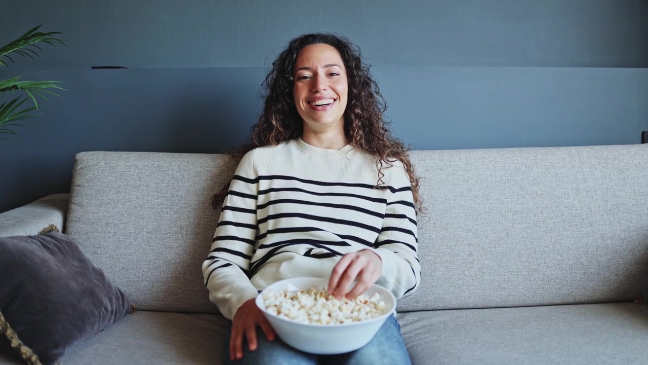 Jovem Mulher Comendo Pipoca Enquanto Assiste Televisão no Sofá