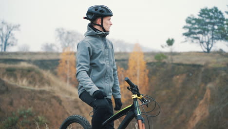 male cyclist putting on a backpack and riding a mountain bike in the hill