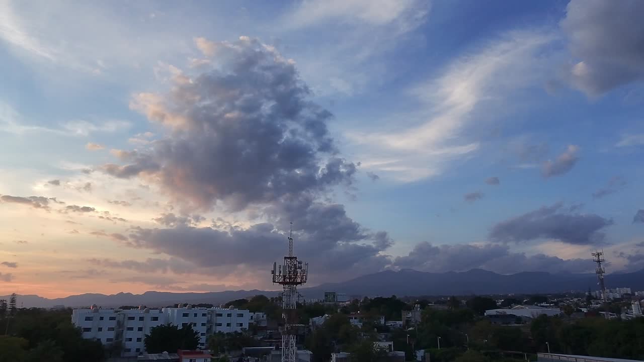 A city skyline with distant mountains under a colorful sunset sky with dramatic clouds.