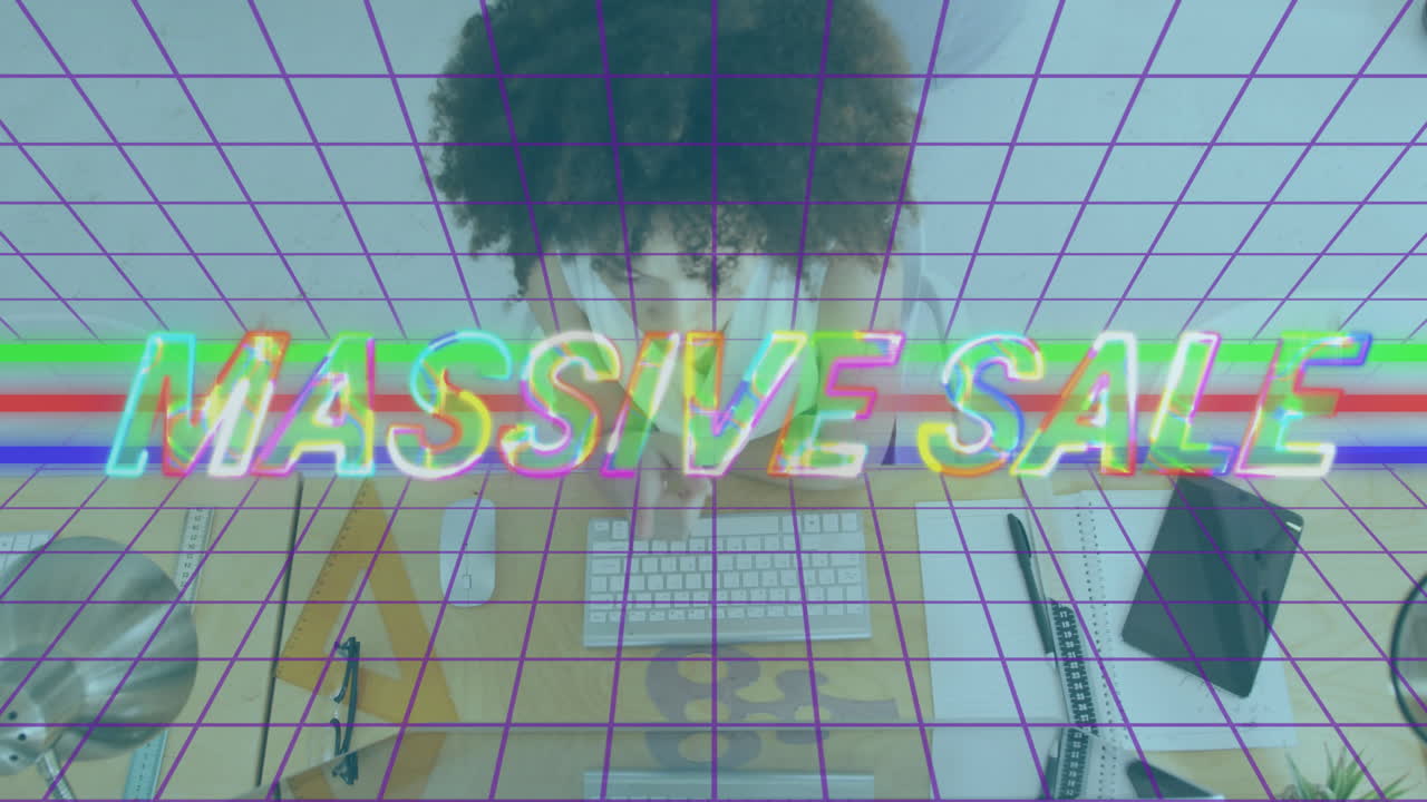 Massive sale text animation over person working at desk with computer