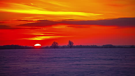tiro de lapso de tiempo de la bola de sol de color naranja que se eleva detrás del campo de invierno cubierto de nieve