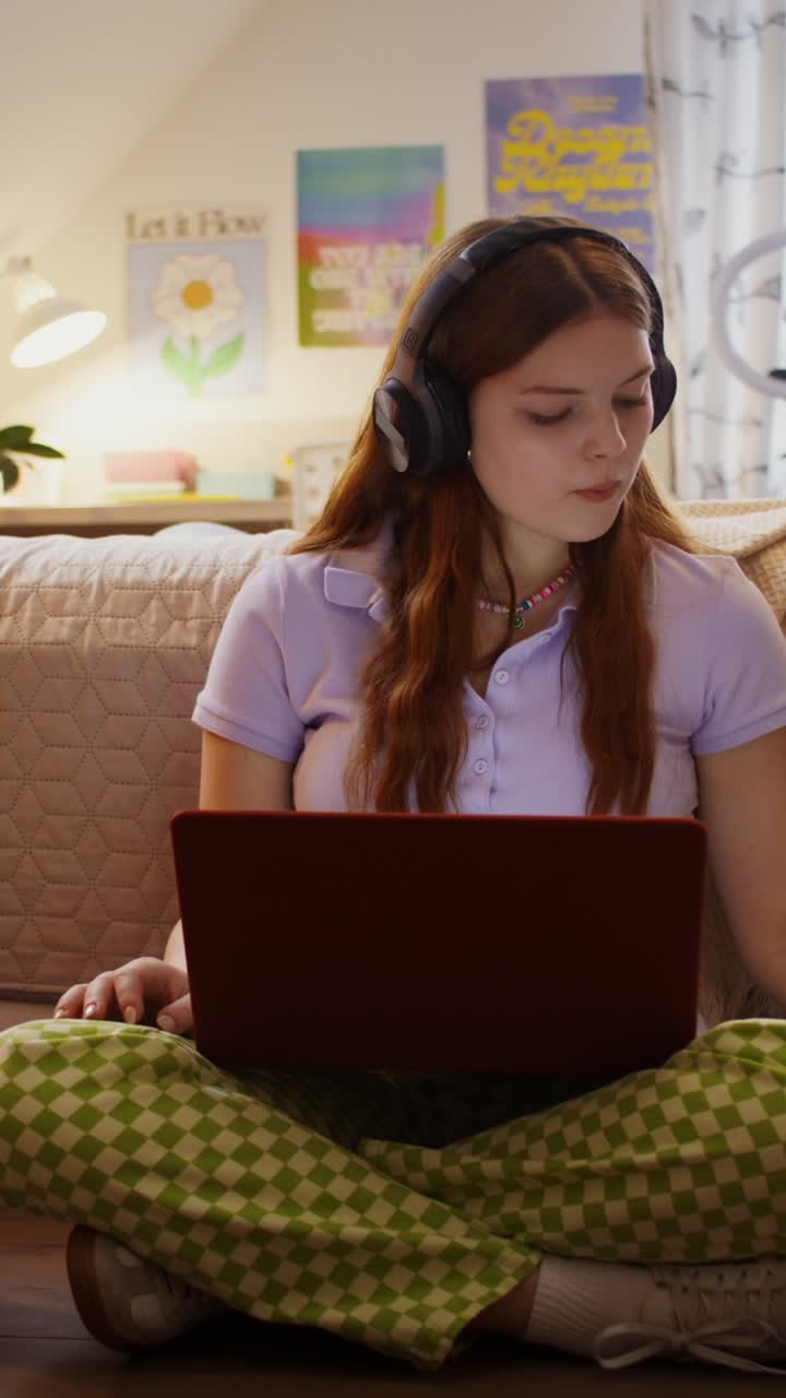 Teenager relaxing at home with headphones, laptop, and drink.