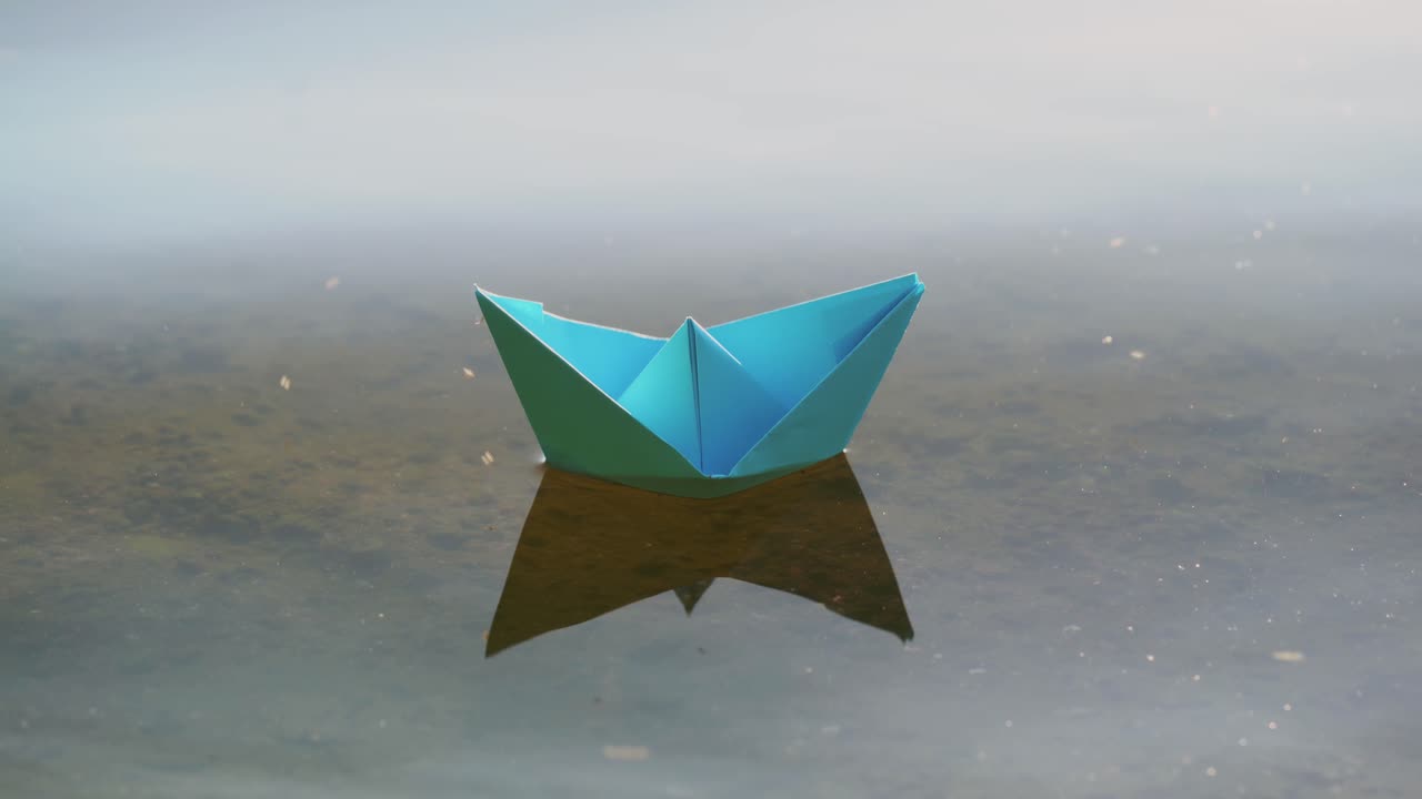 Blue paper boat sailing on water on romantic sunset. Origami.