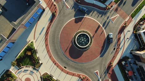 aerial top-down drone shot of traffic circle with cars entering and exiting, decorative brick and water fountain