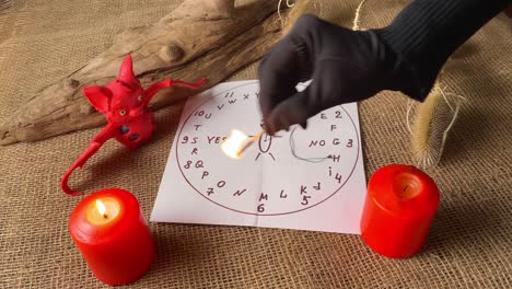 Fortuneteller's black gloved hand burning candles. Preparing for spiritualism ritual. Candle, bat and magic circle in dark room. Mystical atmosphere of fortune telling.