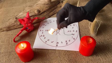 fortuneteller's black gloved hand burning candles. preparing for spiritualism ritual. candle, bat and magic circle in dark room. mystical atmosphere of fortune telling.