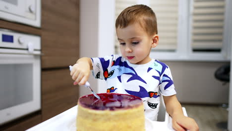 lovely toddler boy puts the fork into a big cake in front of him. parent's hand shows number three candle burning and kid blows it.