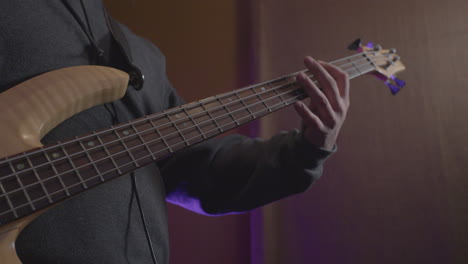 close up of a bass guitarist playing a song on a bass guitar in a recording studio with his band