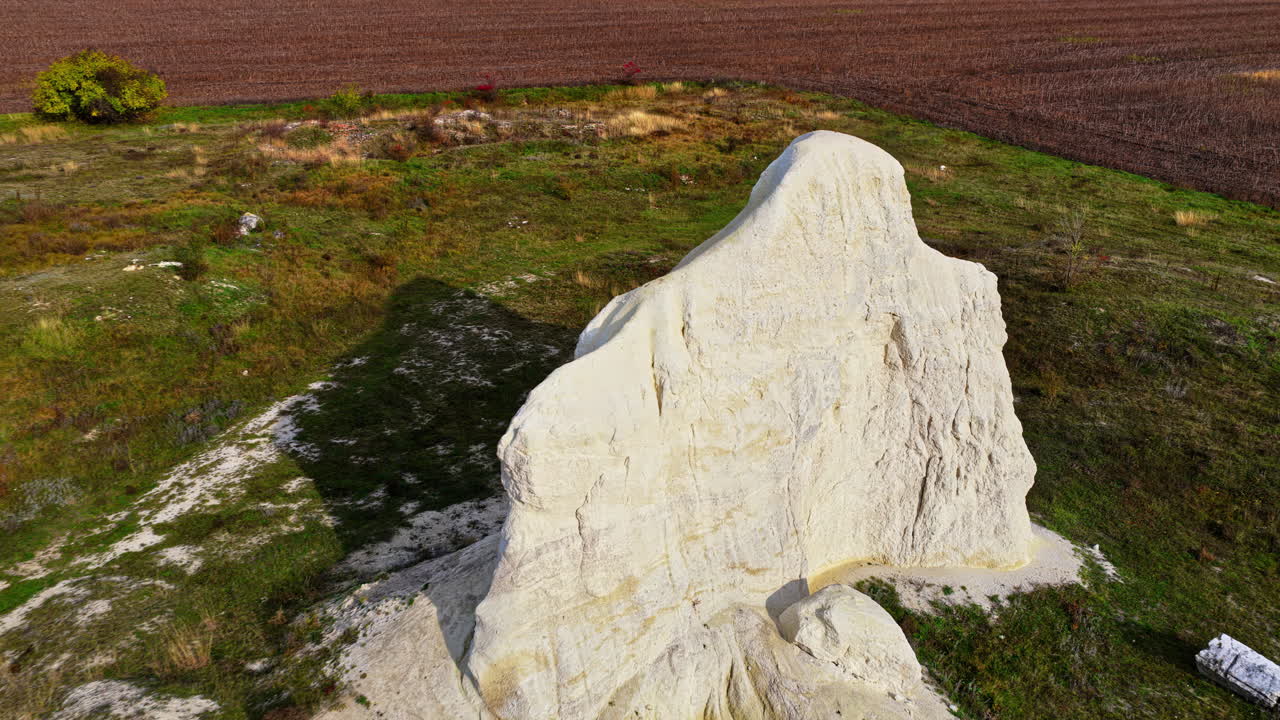 Aerial drone view of a large white chalk rock formation rising from flat Moldovan fields