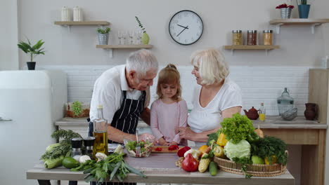 elderly grandparents in kitchen feeding grandchild girl with chopped red pepper. vegetarian diet