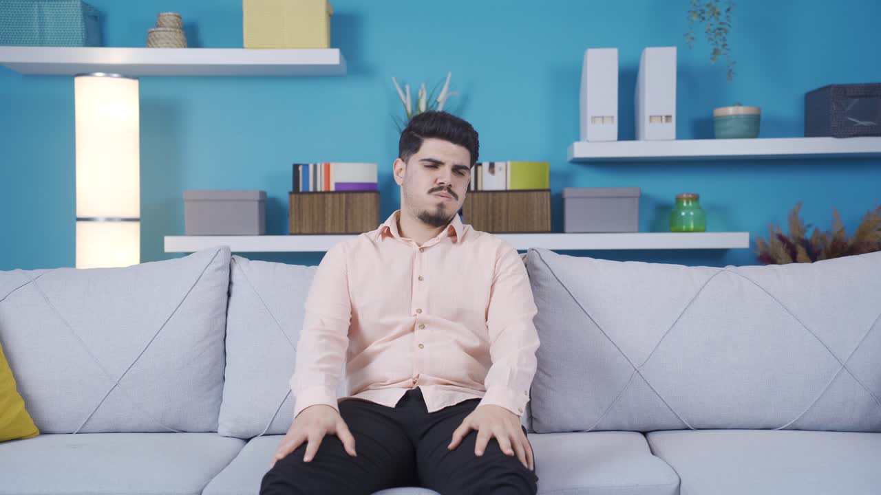 소파에 앉아있는 젊은 남자가 피곤하고 지쳤습니다.