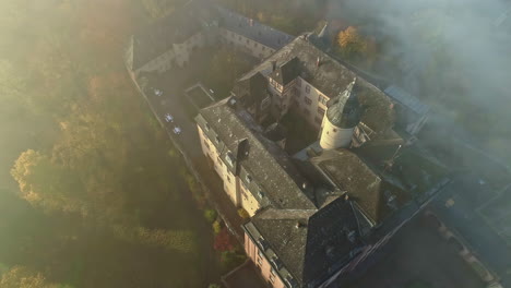 toma aérea de arriba hacia abajo del histórico castillo alemán en una densa niebla durante la puesta de sol