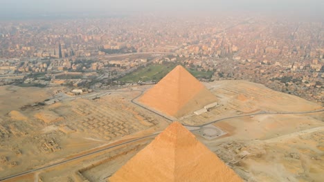 Die-Luftaufnahme-Zeigt-Die-Majestätischen-Pyramiden-Von-Gizeh-Und-Das-Weitläufige-Pyramidenplateau,-Eingerahmt-Von-Wohngebieten-Im-Hintergrund,-Und-Verkörpert-Den-Geist-Des-Reisens-Und-Entdeckens