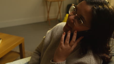 close up of young woman spending evening at home sitting on sofa answering call on mobile phone