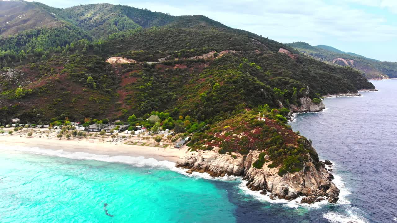 Aerial drone view of the Aegean sea coast with camping near the beach, multiple greenery, hills on the background, blue water with waves. Greece