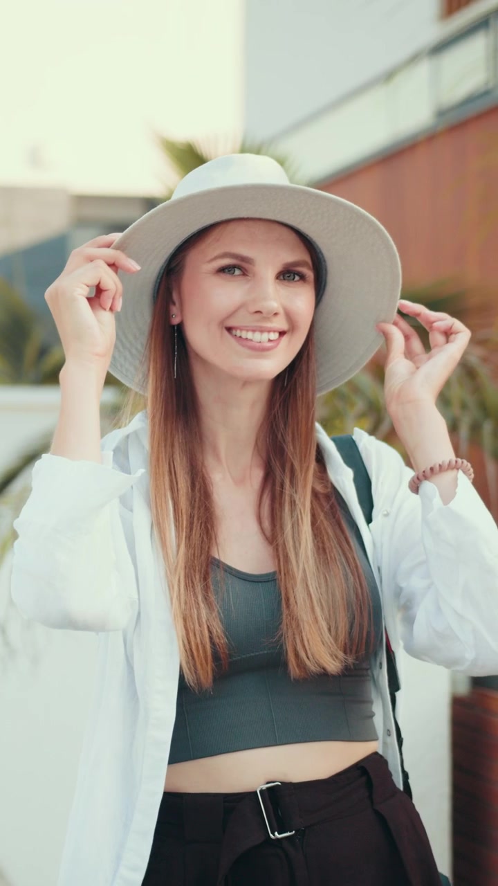Una bella donna con i capelli lunghi sorride mentre indossa occhiali da sole e un cappello; è all'aperto in una giornata di sole.