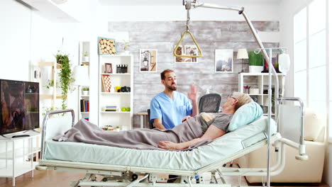 caregiver in retirement home talking with an old lady lying on hospital bed