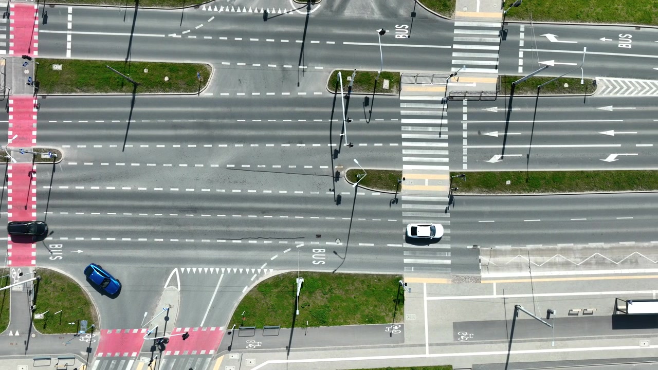 A cinematic topdown aerial shot of a modern city intersection in Gdynia featuring red bike lanes, pedestrian crosswalks, and moving cars.