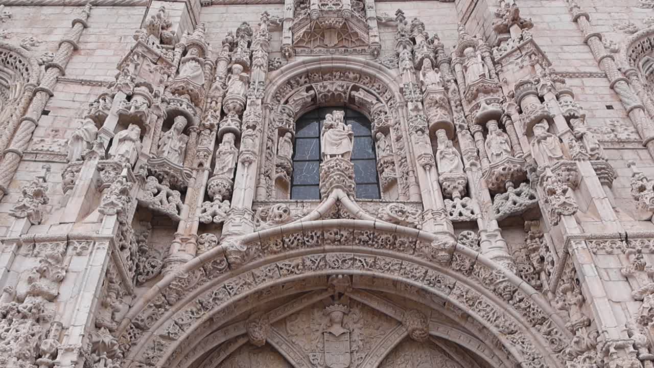 Slow upward pan revealing the ornate stone entrance of Jeronimos Monastery in Lisbon with historic sculptures and detailed Manueline architecture