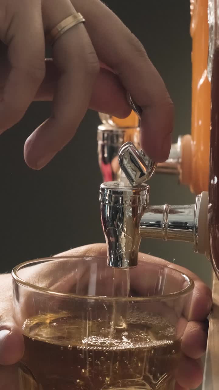 Primo piano di mano che versa una bevanda dorata da un erogatore in un bicchiere