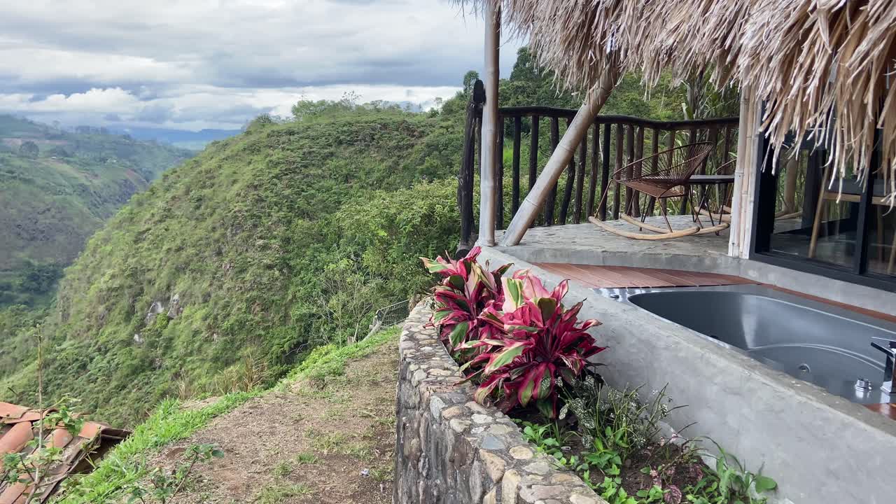 jacuzzi al aire libre en la suite de una cabaña de techo de paja con vistas al verde valle tropical