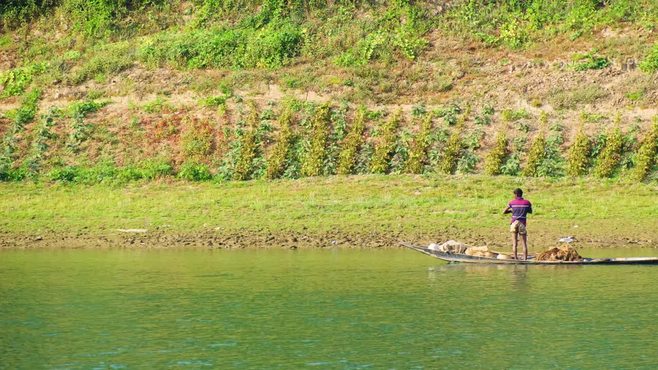 Man paddles flat bottom canoe with long oar while young boy stands on boat