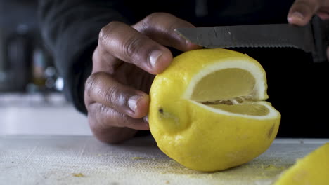 hand of ethnic minority adult male using serrated knife to slice yellow lemon on cutting board