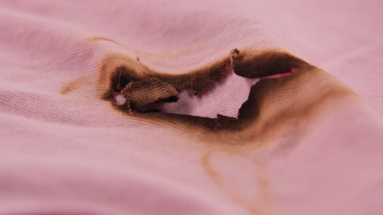 Primo Piano di un Foro Bruciato su Tessuto Rosa