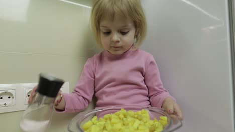 little girl is sitting in the kitchen and preparing a salad