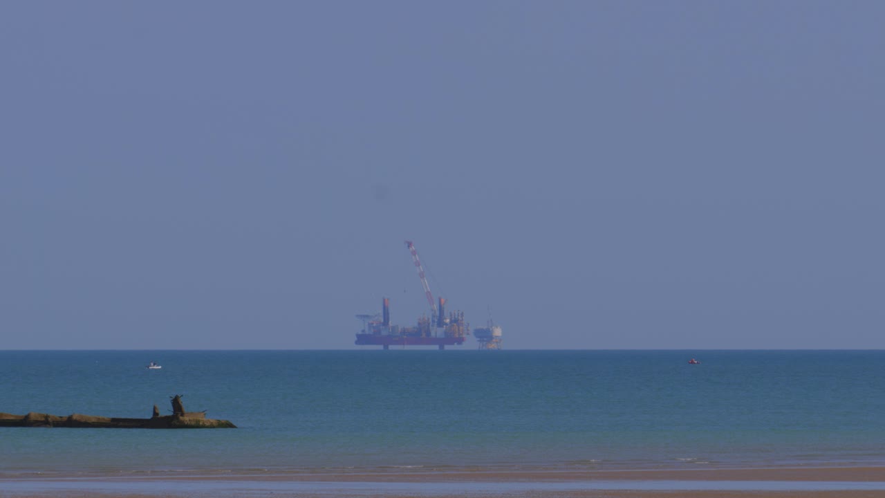 영국 해협에 있는 석유 기지의 모습 - 프랑스 만에서 볼 수 있는 모습 - 은 여름날에 노르망디의 골드 비치, 전면에 2차 세계대전의 인공 항구 잔재가 있다.