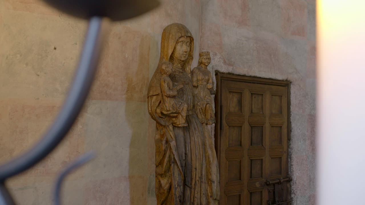 A wooden sculpture depicting a mother with children, viewed through candles