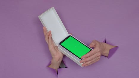 un nuevo teléfono con una pantalla verde en una caja en tus manos, sobre un fondo púrpura