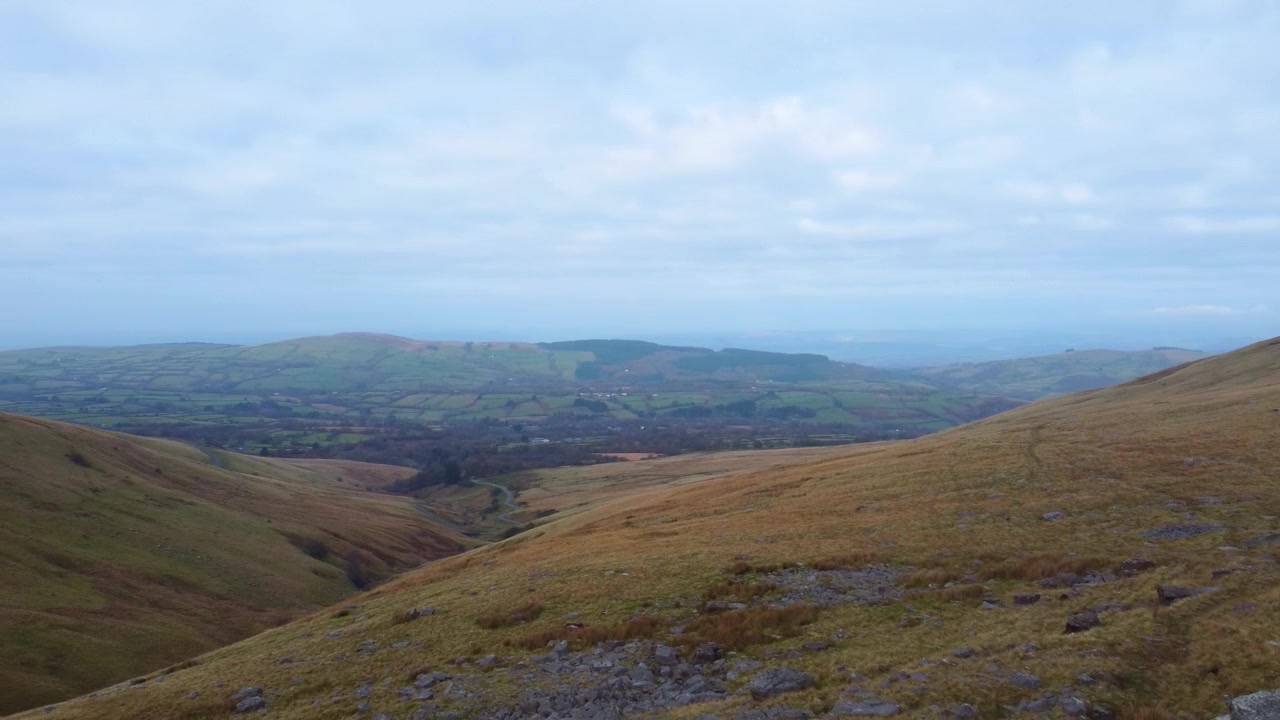 Panorerende luftfoto af Brecon Beacons Bannau Brycheiniog Nationalpark med klipper og dyb kløft, der snor sig ned til landbrugsmarker på en overskyet dag 4K