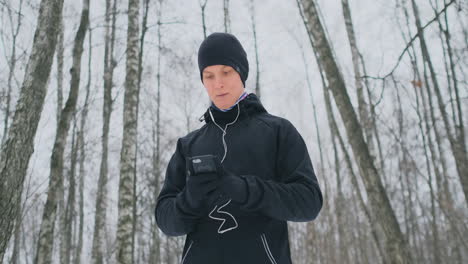 a young man in a black trigger in the winter is preparing to jog in the park includes running music on a smartphone and runs with a voice assistant through the forest doing business and leading a healthy lifestyle