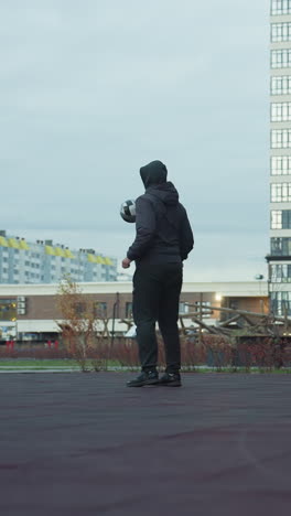 hombre haciendo malabarismos con el fútbol en la arena deportiva durante la sesión de práctica, el fondo incluye edificios urbanos, patio de recreo, vegetación y elementos al aire libre