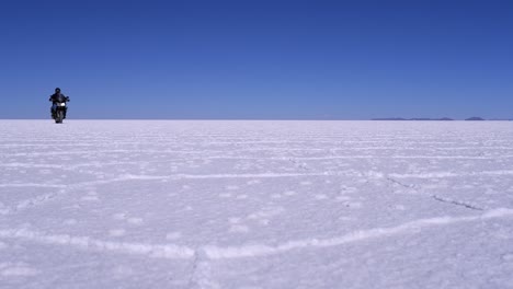 Motorcyclist-rides-diagonally-into-frame-on-Uyuni-Salt-Lake-Flat,-BOL