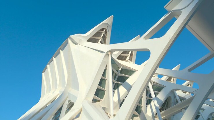 Futuristic white architectural landmark with sweeping angular supports, glazed surfaces, and pointed rooflike forms under clear blue sky, with architecture, building, modern, futuristic detail