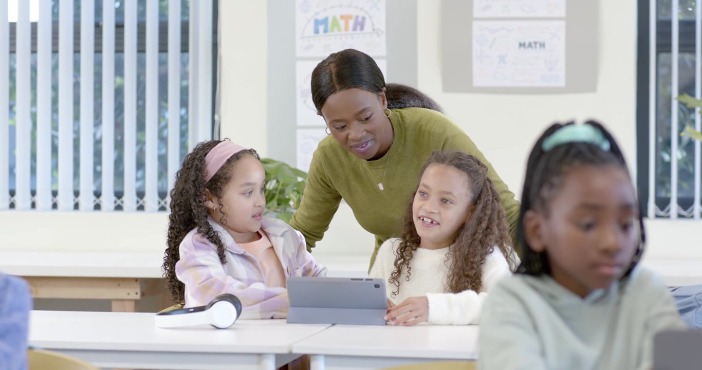 Insegnante donna afroamericana che guida le studentesse dopo aver toccato i tablet sui banchi per la lezione di matematica