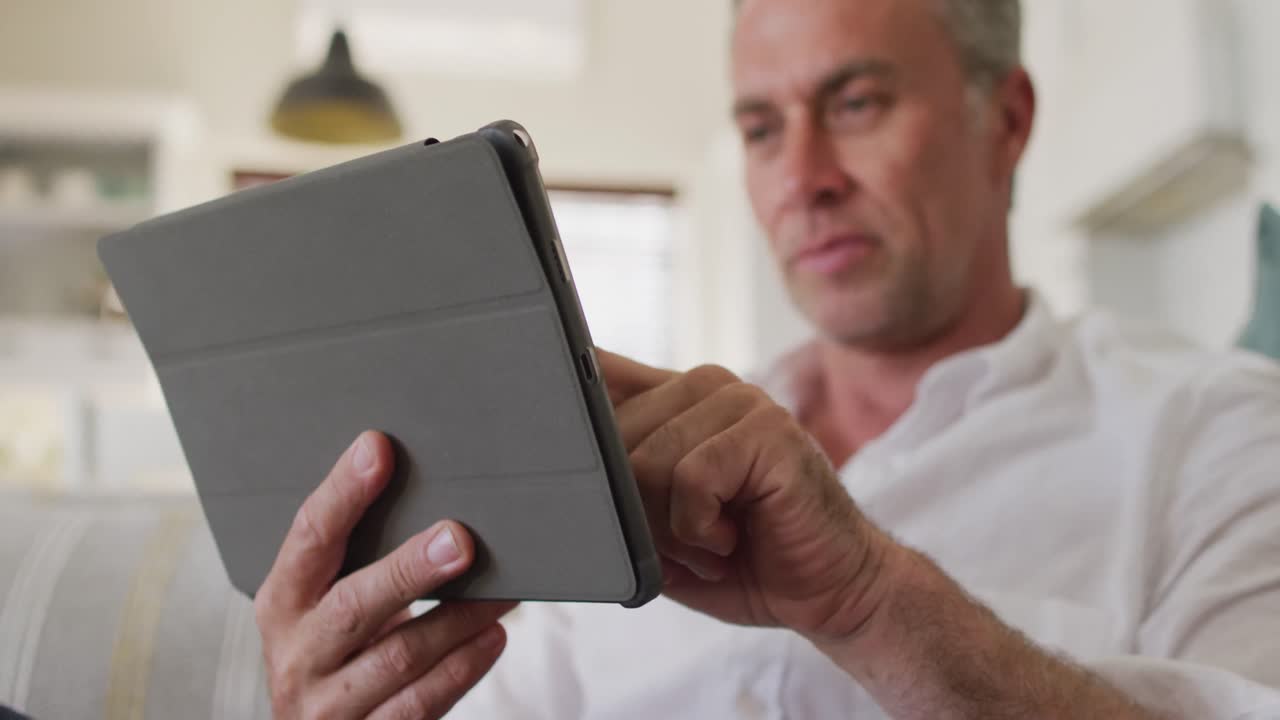 hombre caucásico feliz sentado en el sofá en la sala de estar, usando una tableta