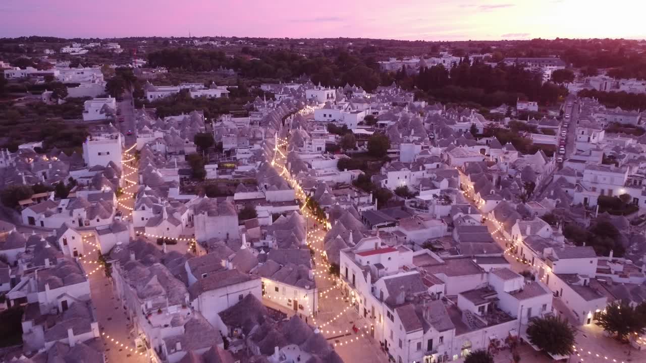Alberobello, Puglia, Italy - Aerial Drone View by Sunset - Trulli, Old Town and Lights turning on while flying