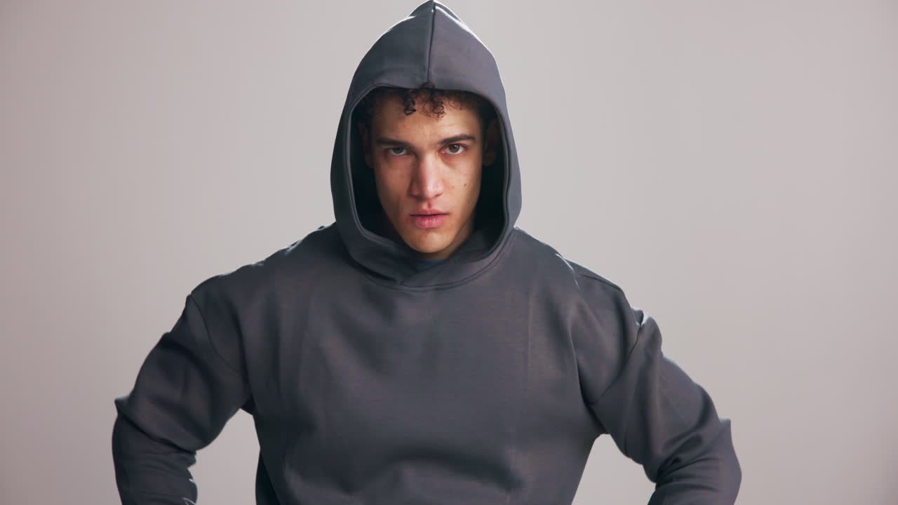 Ung man som drar upp huvan på en grå hoodie med ett allvarligt uttryck