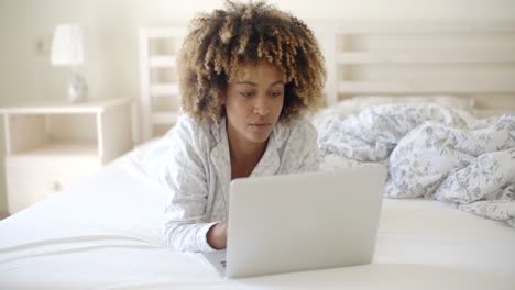 mujer mirando la computadora portátil en la cama en casa